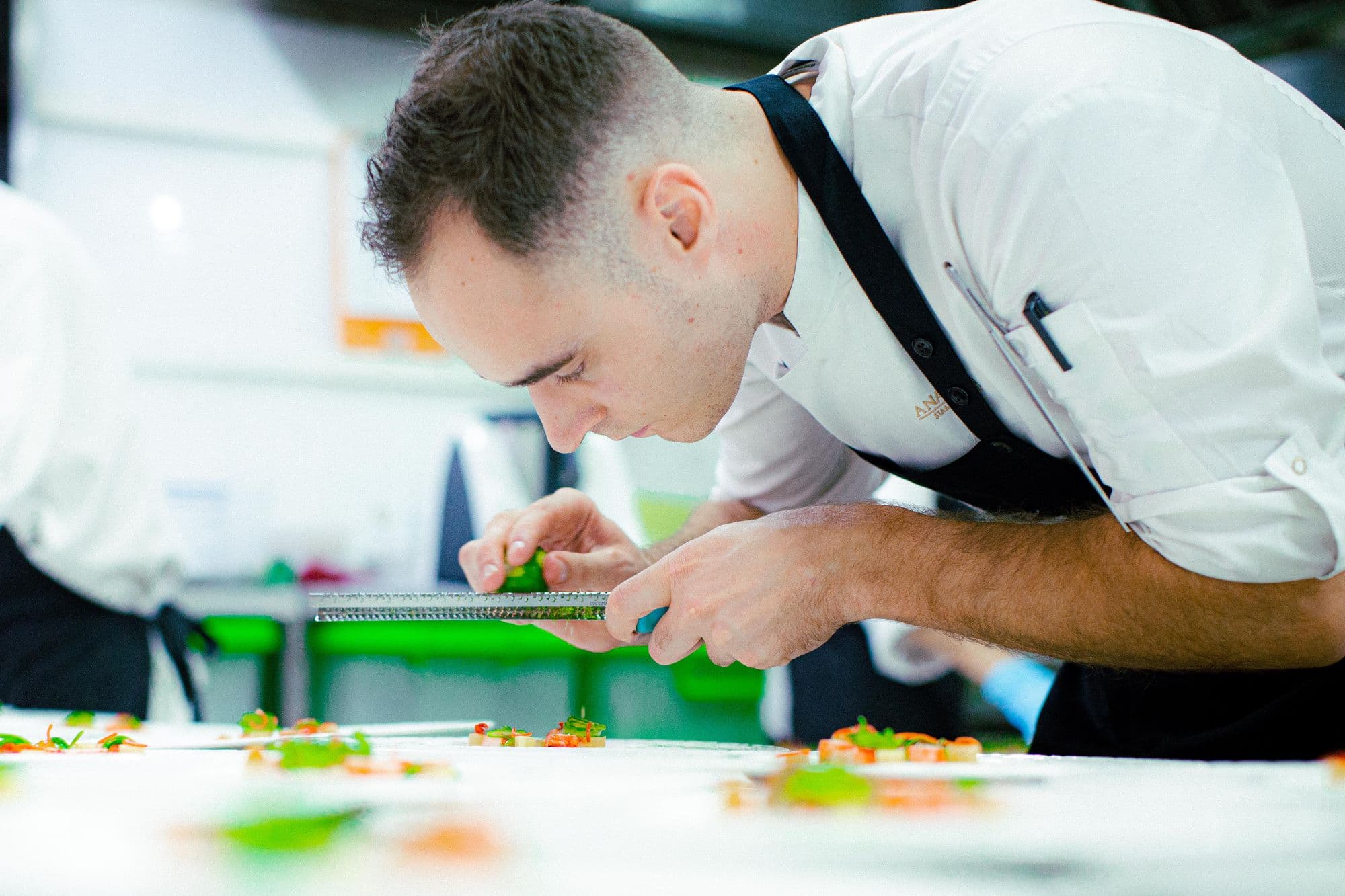 Chef using a microplane to finish plated dishes in a professional kitchen