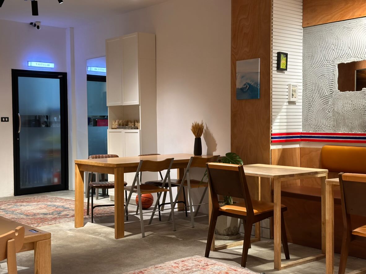Interior of a modern, cozy island café in Phuket with wooden tables, ambient lighting, and a view of the “Tasty Lab” door in the background.