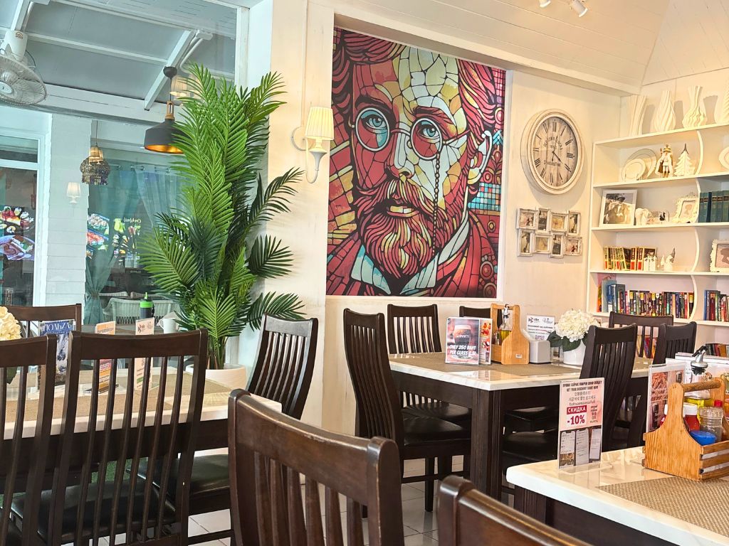 Bright interior of Chekhoff Restaurant in Kata Karon with wooden tables, bookshelves, and colourful portrait artwork.