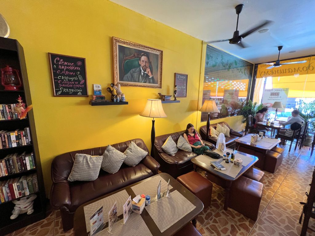 Lounge seating area inside Chekhoff Restaurant in Kata Karon with leather sofas, yellow walls, and bookshelf décor.