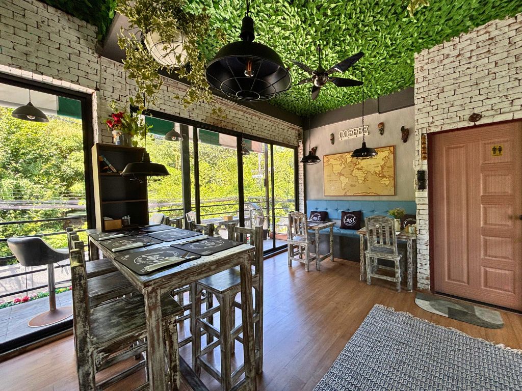 Second floor seating area at Lost in Phuket café with leafy ceiling, rustic furniture, and balcony views in Kata Karon.