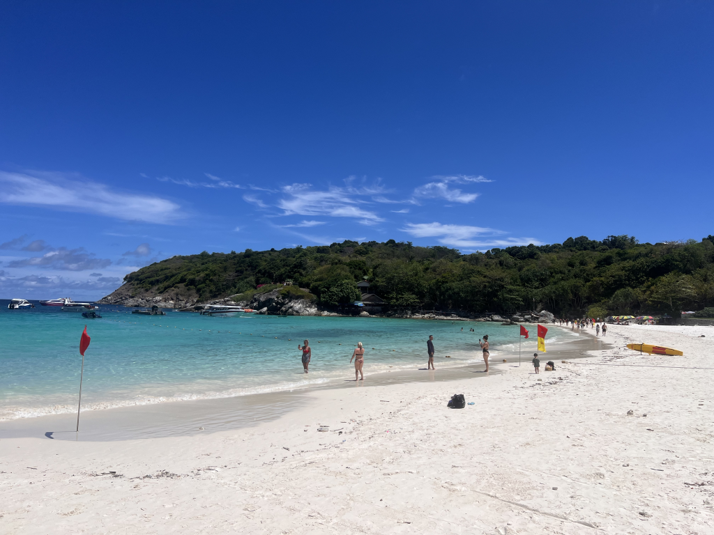 Tourists enjoying the white sand beach and turquoise waters of Racha Yai Island, a top island hopping destination near Phuket.