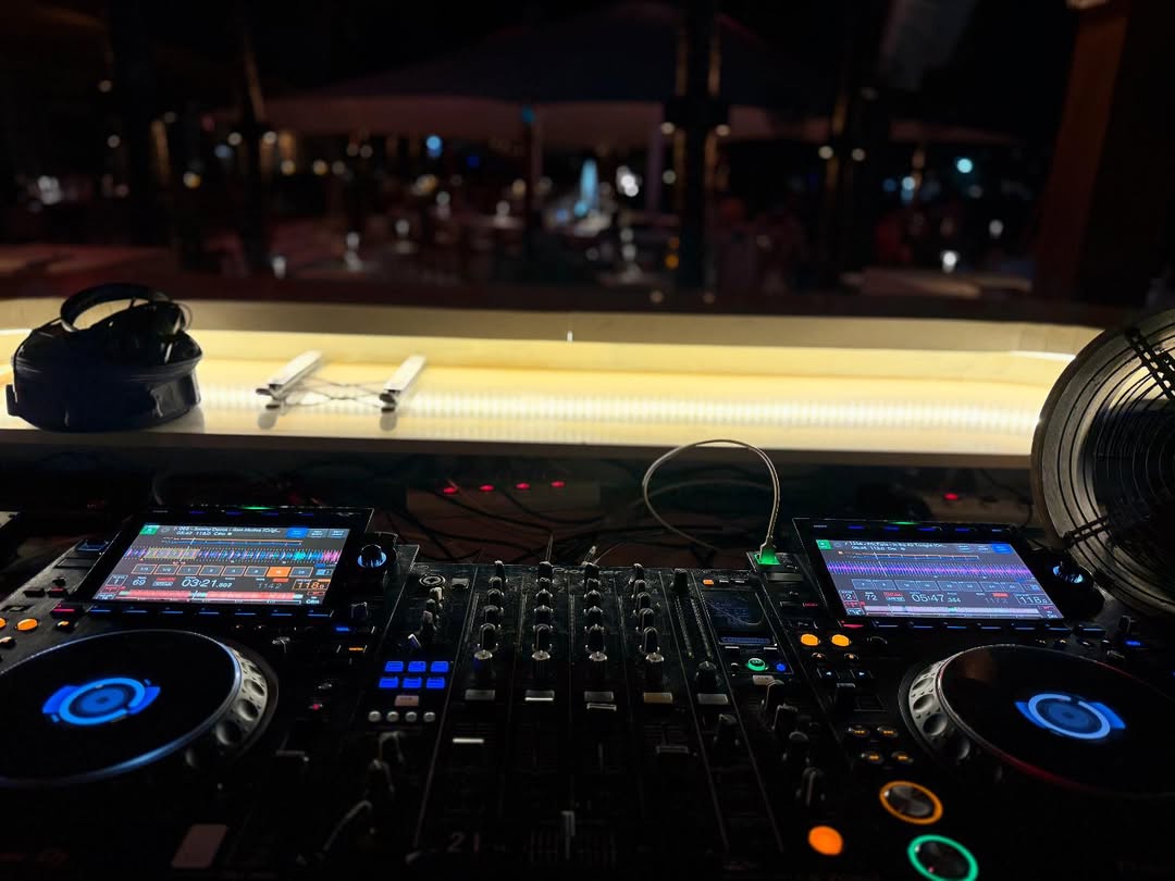 DJ booth at a beach club in Phuket at night, with colourful LED decks and a blurred party atmosphere in the background