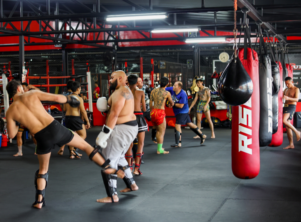 Muay Thai fighters sparring at Maximum Fitness Phuket gym with red punching bags and boxing ring