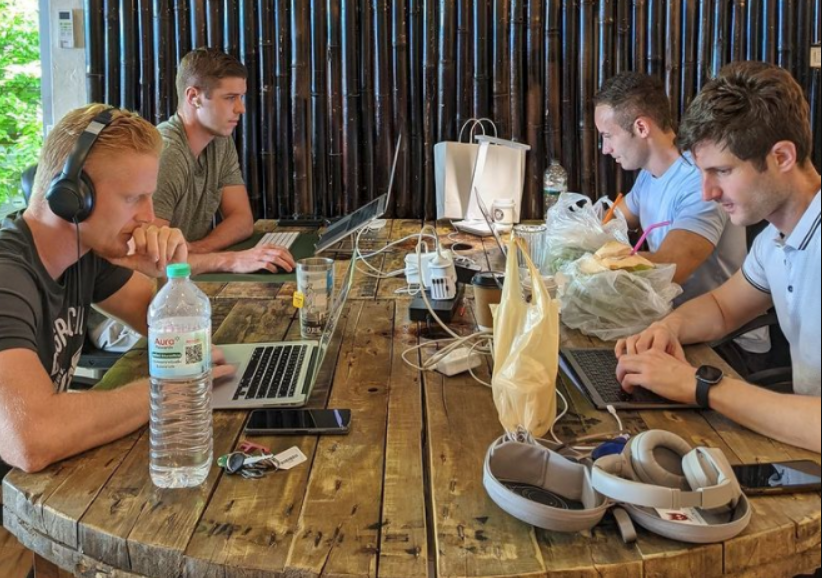 Group of digital nomads working on laptops at a shared coworking table in Phuket, Thailand